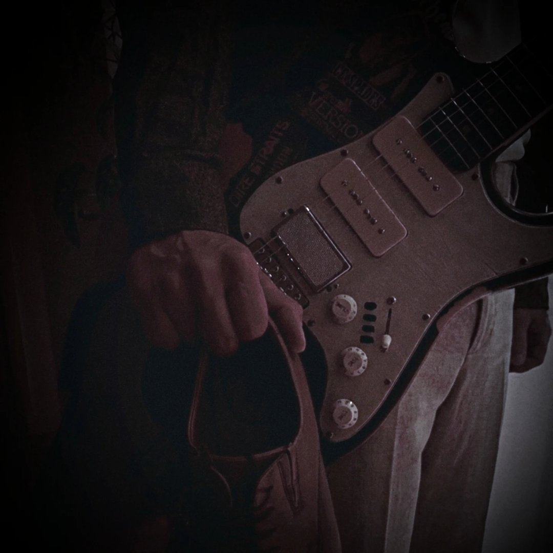 A hand holding a shoe in front of an electric guitar